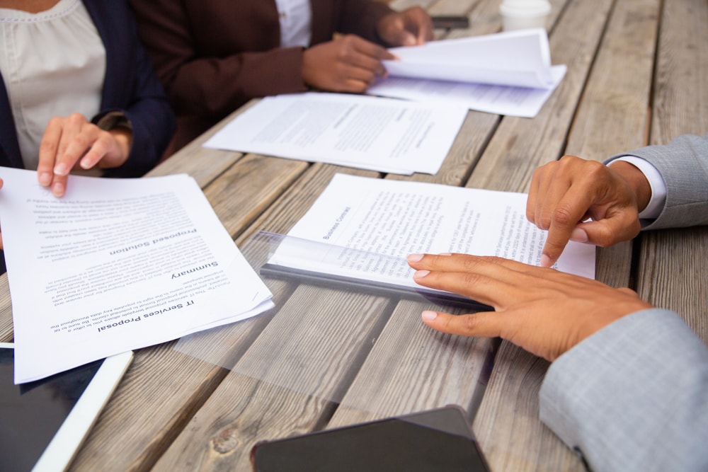 Pessoas estudando documentos em cima de uma mesa.